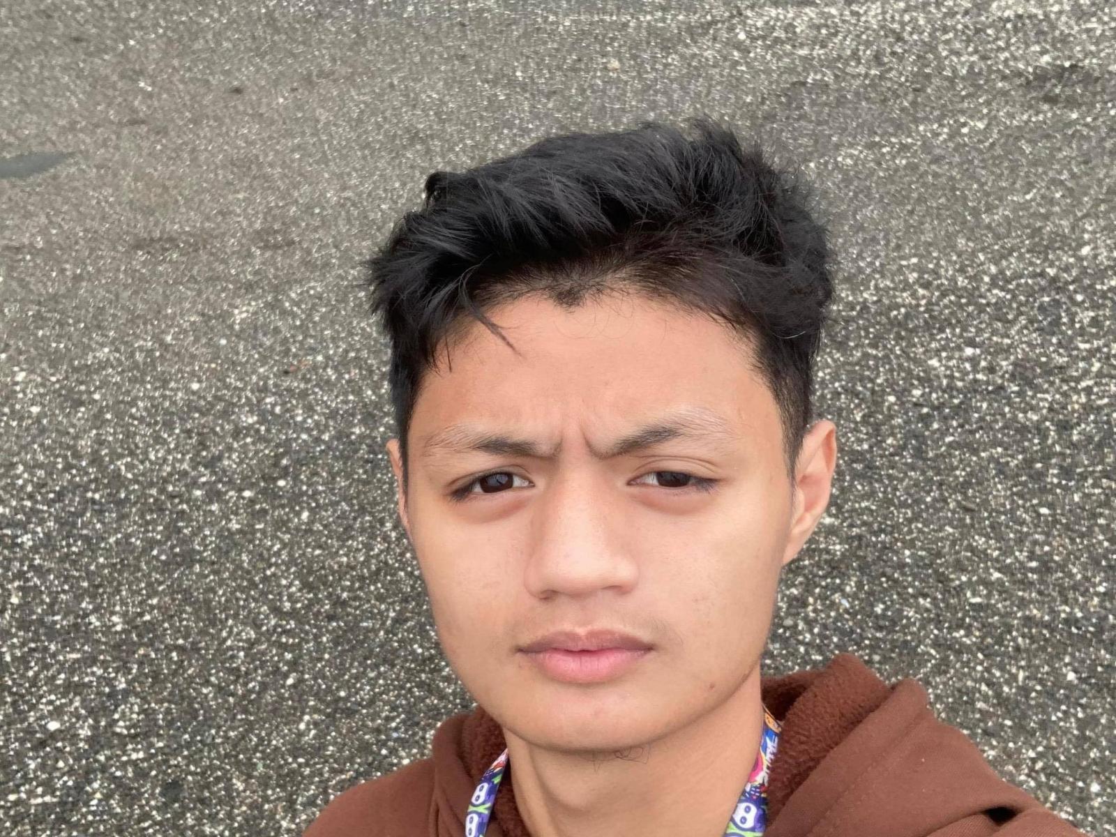 LucasSoHot has a neutral, slightly annoyed expression, short black hair, and is wearing a brown hoodie with a colorful necklace. His face is slightly sweaty.
