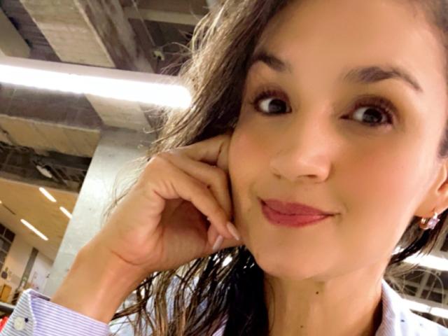 SofiaVerlek has brown eyes, long brown hair, and is smiling with pink lips. She's touching her cheek with her right hand, wearing a striped shirt.