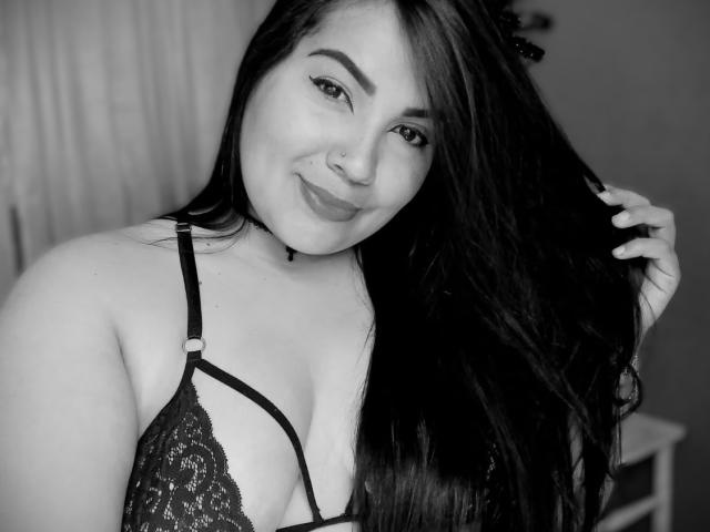AvaChanne with long dark hair, smiling, wearing black lace bra, holding hair, nose ring, and makeup, showing her tits and a cute, sexy face in a black-and-white photo.