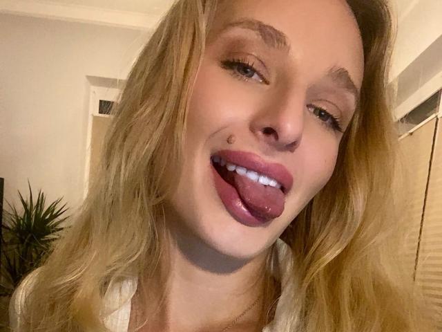 Marilyn: Cabelos loiros, piscando, língua de fora e uma pequena marca de beleza na bochecha esquerda. Ela está usando batom rosa e uma camisa branca..