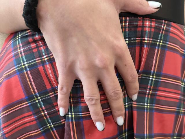 Stefanni's hand with white nails rests on her red and blue plaid butt, wearing a black scrunchie on her wrist. Her fingers are slightly spread.