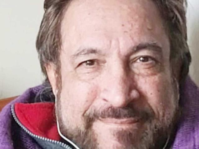 LeonMacK has a chubby face, brown eyes, thin mustache, and a slight smile. He's wearing a purple jacket with a red lining. His hair is brown and wavy.