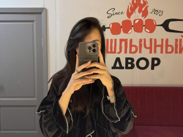 LillianSunny with long dark hair, wearing a black robe, holding a phone in front of her face, taking a mirror selfie, visible ass, ring on her left hand.