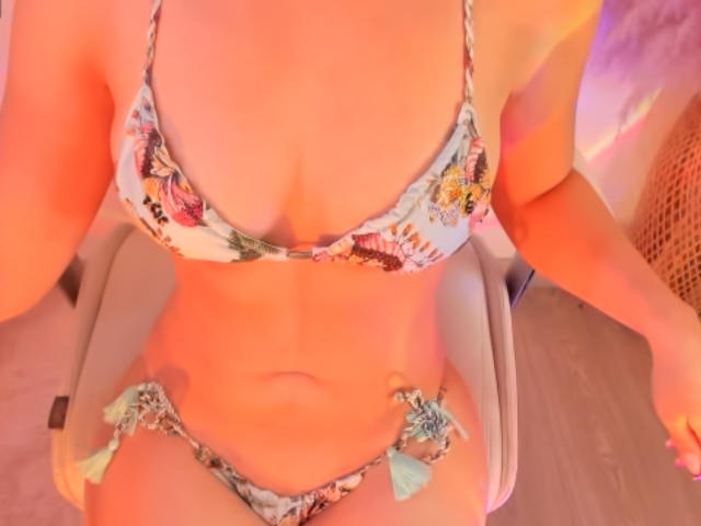 LinsayColemann wearing a floral bikini with tassels, her tits are small to medium, her belly is exposed, and she's sitting on a white chair, her pussy is not visible.