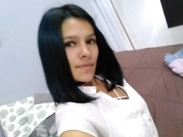 AmelieBlake has black shoulder-length hair, a nose ring, and is wearing a white button-up shirt. Her small tits are slightly visible under the shirt. She's smiling.