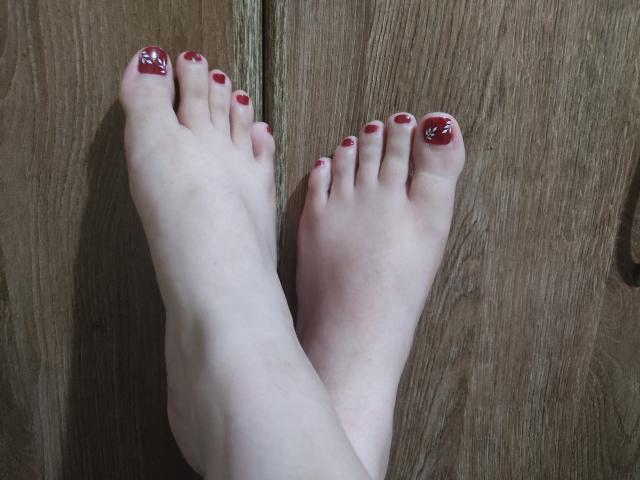 JackyEmma's bare feet with red nail polish, featuring white swirls on the big toes, resting on a wooden surface.