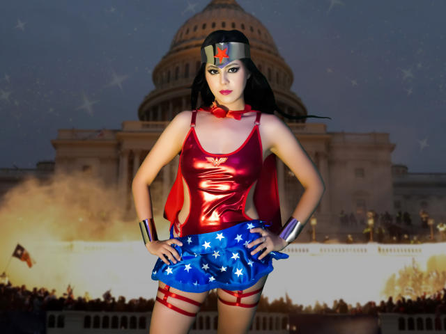 EimmyPark in a shiny red top, blue star-spangled skirt, and red boots, standing with hands on hips, wearing a silver headband, black hair, and metallic bracelets.
