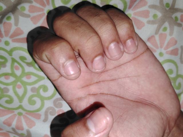 Jorzo's hand with short, clean fingernails, slightly curled fingers, and a light brown skin tone. Background has a patterned design. Jorzo's thumb is on top, index on bottom.
