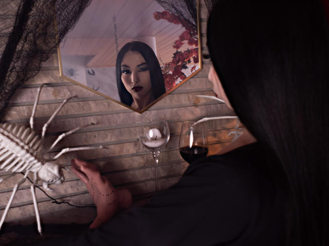 Camille Rios, con i capelli scuri, un abito nero e il rossetto rosso, fissa il suo riflesso in uno specchio. In primo piano, c'è un bicchiere di vino rosso e uno scheletro..