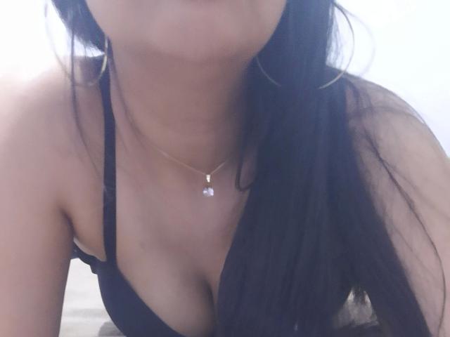Mellinda-hot with black hair, wearing a black bra, showing her tits, gold necklace with a small pendant, and large hoop earrings, in a slightly blurred, intimate selfie.