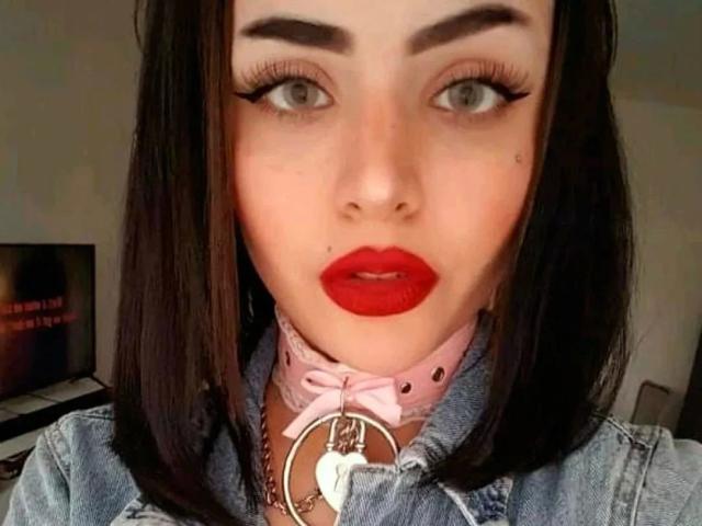 Celestia-hot has pale skin, red lipstick, dark eyebrows, long eyelashes, and a pink collar with a metal ring and white heart, wearing a denim jacket.