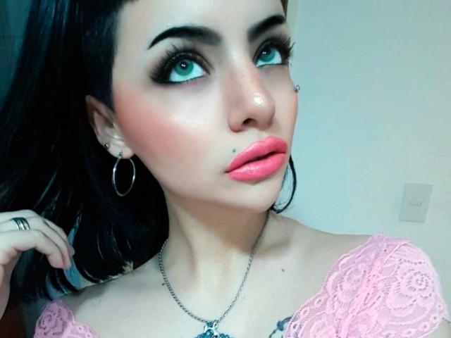 Celestia-hot with pale skin, dark hair, green eyes, pink lipstick, black eyeliner, hoop earrings, pink lace top, nose piercing, and necklace, looking up with a subtle smile.