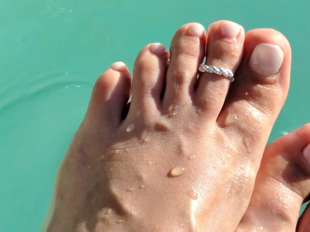 MistressMica's wet foot with small droplets, showing a diamond ring on the second toe, against a turquoise background. Her toes are slightly curled and her nails are neat.