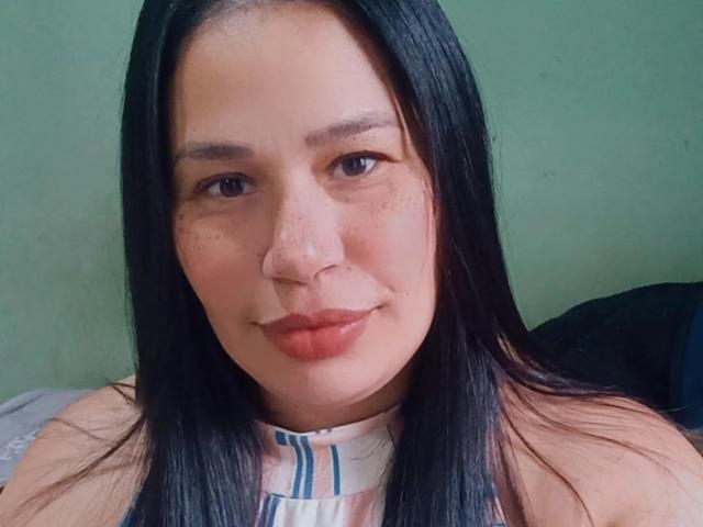 Nicole69s has long black hair, freckled face, and full red lips with a slight smile. She's wearing a striped sleeveless top, and her nose is pierced.
