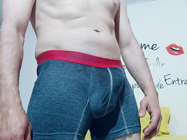 FernandoAndIsabella's slim, shirtless torso with grey boxer shorts and red "PUMA" waistband, showing a visible bulge in the crotch area. Hands by sides, pale skin.