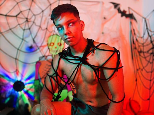 EdwinBlaze with a muscular, shirtless body, black rope webbing across his chest and arms, red and blue lighting on his face, and a stuffed green toy in the background.