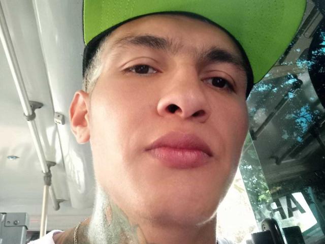 AbrahamStiff has a medium skin tone, short dark hair, and a green backward baseball cap. His lips are slightly pouted, and he's looking into the camera.