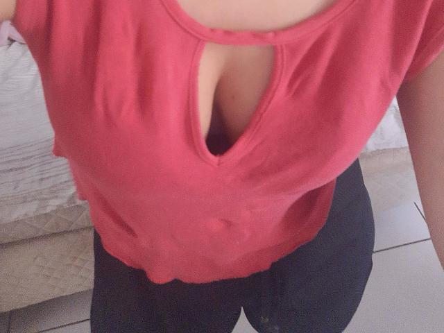 Mellinda-hot's pink top has a deep cleavage cutout, showing her tits, with black pants below. Her skin is light, and the image is a selfie.