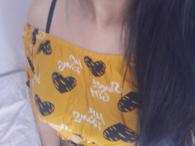 Mellinda-hot's yellow off-shoulder top with black heart and white text patterns, showing her small tits and black strap, with long dark hair on the right side.