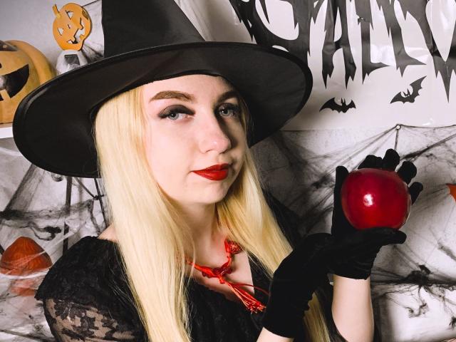 BeatriceFly with blonde hair, black witch hat, red lipstick, black lace shirt, black gloves, holding red apple, pale skin, sexy, Halloween costume, holding apple in right hand.