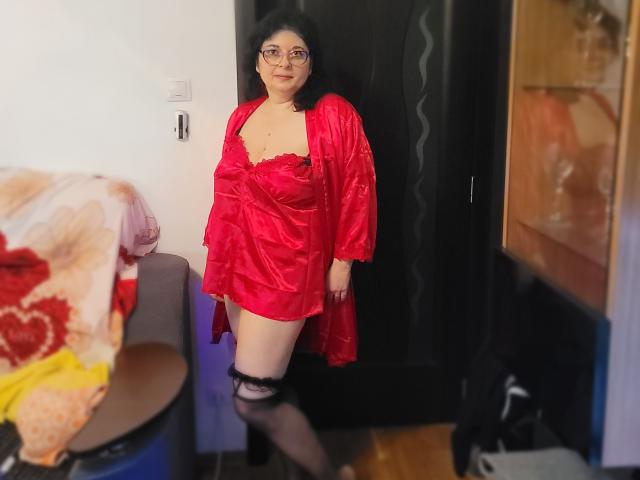 HotAndSexyMature with pale skin, black curly hair, glasses, red satin dress, black lace thigh high, standing in doorway, slightly smiling, showing small tits, black door behind.