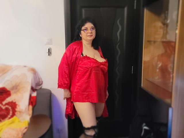 HotAndSexyMature with black curly hair, glasses, red satin robe, and lace lingerie, standing in doorway, showing her tits and bare ass, looking confident.