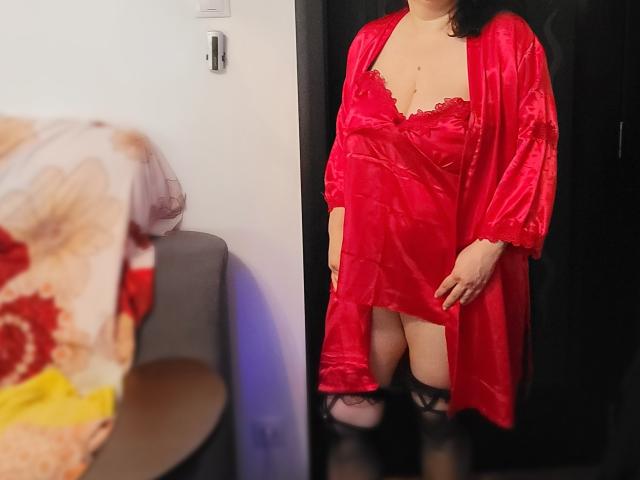 HotAndSexyMature in a red satin robe with lace trim, exposing her tits, wearing black thigh-highs, standing in a dark doorway, reflecting in a mirror.