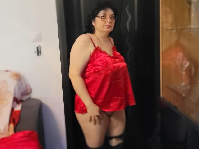 HotAndSexyMature with pale skin, black curly hair, glasses, red satin lingerie, exposed black thong, and black stockings, standing in a doorway, looking slightly annoyed.