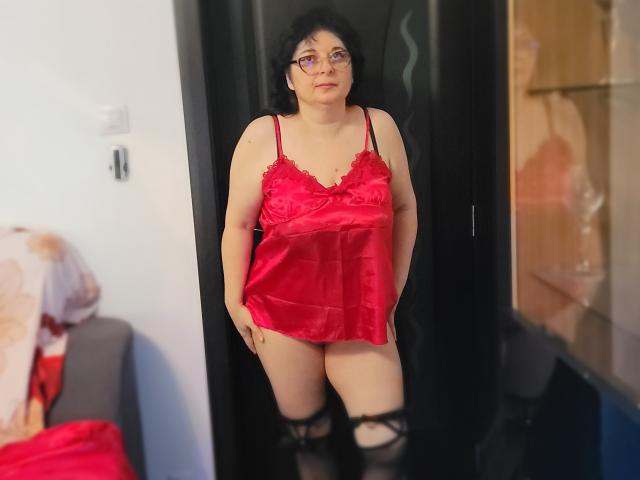 HotAndSexyMature with dark curly hair, glasses, red satin lingerie, black thigh-high stockings, standing in doorway, showing small tits and a chubby ass.