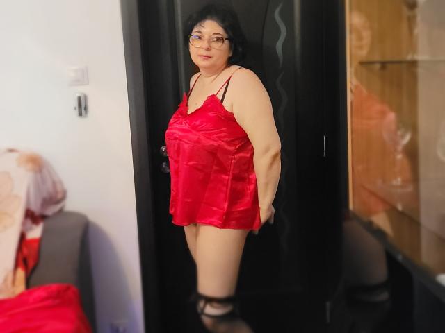 HotAndSexyMature, chubby with black hair, wearing red satin lingerie, standing in black door frame, looking at camera, glasses on, black stockings, subtle smile, bedroom setting.