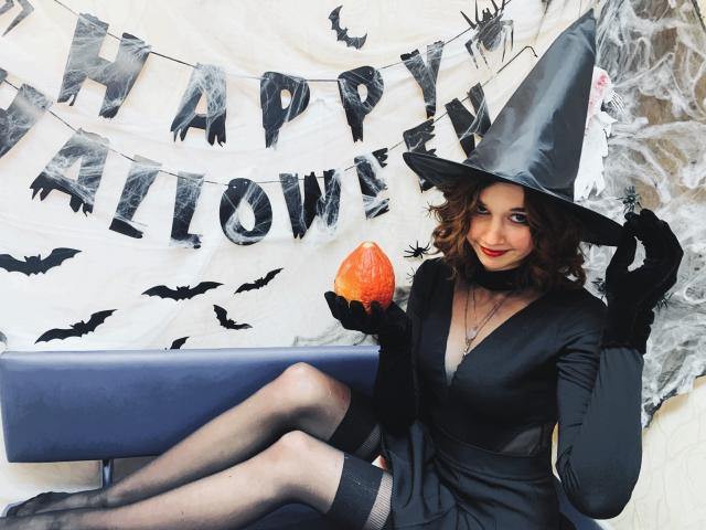 LettyCurly, witch costume, gray hat, black dress, black gloves, holding orange pumpkin, sitting on blue bench, winking, curly brown hair, red lipstick, black stockings, cute, sexy.
