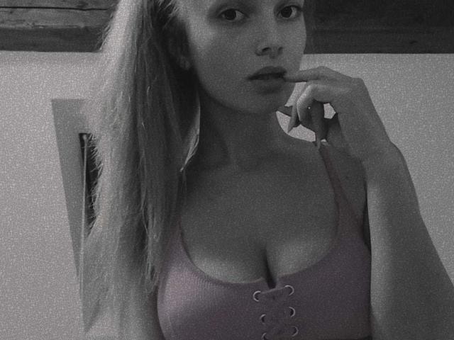 Ingrid, mit langen blonden Haaren, voller Lippen und Finger im Mund, trägt ein rosa gestreiftes Oberteil mit Schnürung vorne, das ihre Brüste zeigt, auf einem Schwarz-Weiß-Foto..