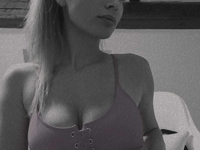 IngridI with medium tits, wearing a pink lace-up tank top, showing cleavage, blonde hair in a ponytail, partial face, in a grayscale photo.