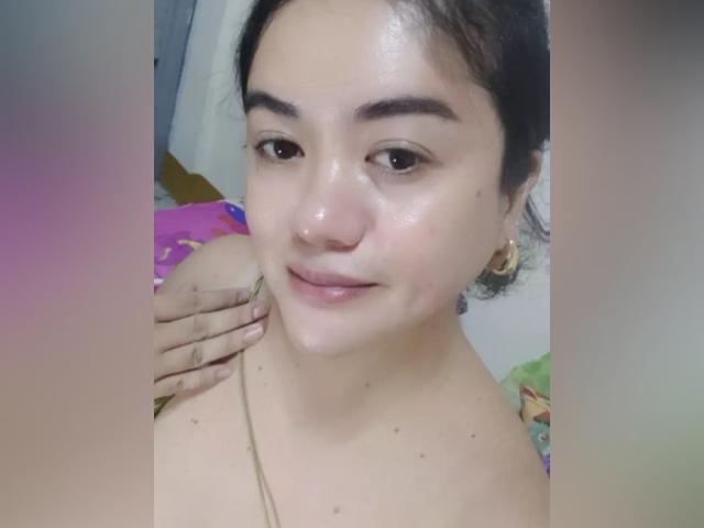 YourSophie has a shiny face, small dark eyebrows, and a subtle smile with a hand on her shoulder, showing her bare shoulders and small dark moles.