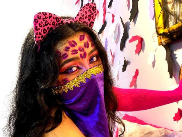 AishaGhulam with leopard bow, purple mask, and leopard face paint, showing tits, with long black hair, purple and gold eyes, and a purple mask with gold trim.