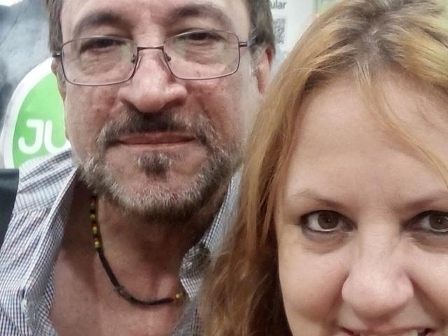 AmantsChauds, con barba e occhiali, e una donna con i capelli rossi e un viso carino, entrambi sorridono alla macchina fotografica. AmantsChauds indossa una camicia a quadri e una collana di perline..