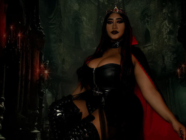 MelisaJackie with large boobs, wearing black leather dress, red cape, crown, black thigh-high boots, dark lipstick, and a choker, sitting in a dark, gothic-style room.