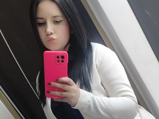 Kkatalina with black hair, white long-sleeve shirt, pink phone, dark nail polish, pouting lips, taking selfie in mirror. Boobs not visible. Ass not visible. Pussy not visible.