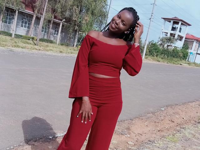 BlackMelanie, em pé, sorrindo, vestindo uma blusa cropped vermelha com um ombro à mostra e calças de cintura alta, com a mão no cabelo trançado, estrada à frente, ensolarado, sua nádega ligeiramente visível, confiante..