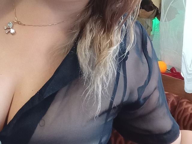 Le haut noir transparent de KelliRedhaer révèle ses seins à travers le tissu, avec ses cheveux blonds et ondulés tombant sur son épaule. Elle porte un collier en or avec de petits pendentifs..