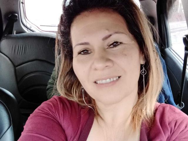 LesbiaThreeBebes tiene la piel de color marrón claro, cabello castaño de longitud media con puntas rubias, ojos marrones, una nariz pequeña, está sonriendo mostrando dientes blancos, lleva una camisa rosa y aretes de aro..