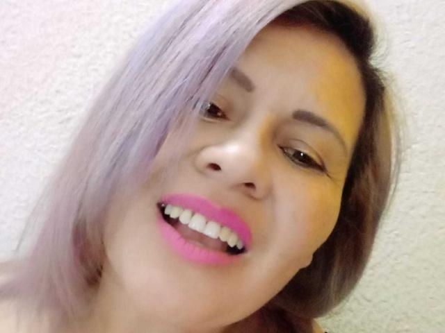 LesbiaThreeBebes con rossetto rosa, sorridenti, che mostrano i denti bianchi, pelle color nocciola, capelli viola e occhi marroni, su uno sfondo di una parete bianca con texture..