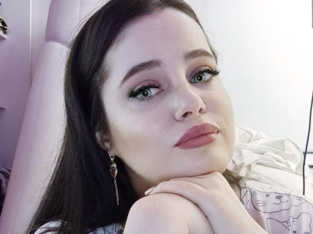 Marizel, con cabello negro largo, ojos verdes y lápiz labial rosa, apoyando el mentón en la rodilla, con aretes colgantes, mirando a la cámara con una ligera sonrisa..