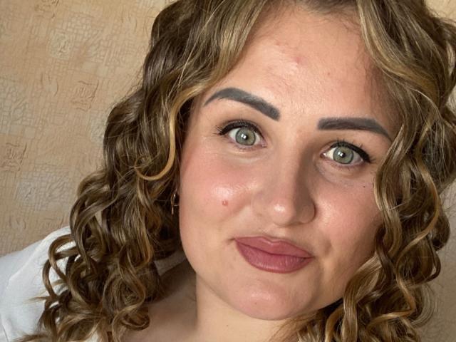 HoneydewWaves hat lockiges, braunes Haar, grüne Augen, dicke Augenbrauen, pinken Lippenstift, einen kleinen Muttermal auf ihrer linken Wange und ein weißes Hemd. Ihr Gesicht ist leicht gerötet..