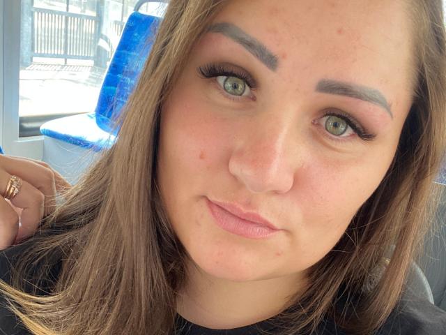 HoneydewWaves tiene el cabello castaño claro, ojos verdes y cejas pobladas. Lleva delineador negro y lápiz labial rosa. Está mirando a la cámara con una ligera sonrisa..