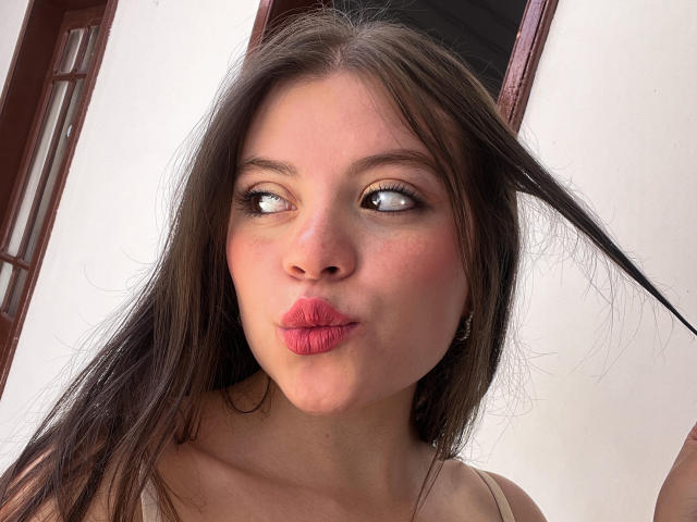 VictoriaAngels with pouty pink lips, brown eyes looking sideways, long brown hair, slightly flushed skin, small nose, wearing a beige top, holding a hair strand.