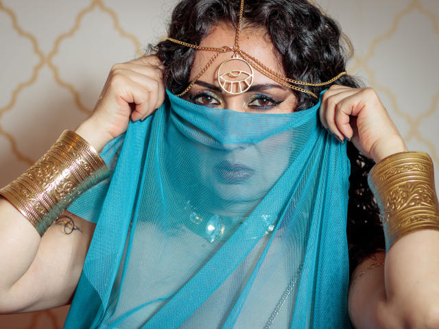 SamanthaAntolin with dark curly hair, gold jewelry, and blue sheer fabric covering her face and tits, holding it up to reveal her tits and a gold necklace.