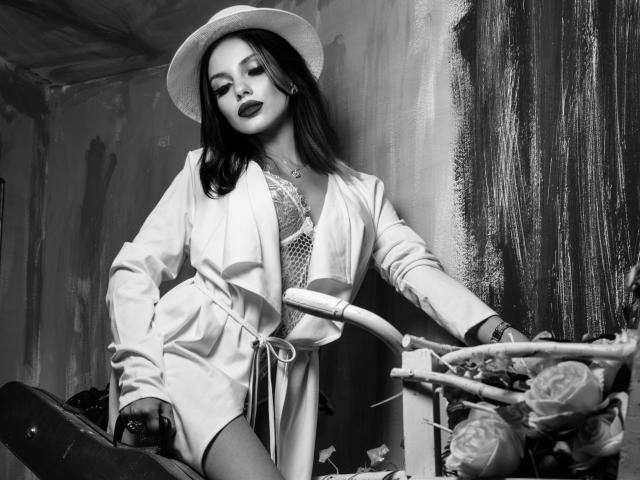 GoddessKaterina with dark lipstick, wearing a white hat, open shirt, and lace bra, leaning on a bike, showing her tits, with a basket of roses in the foreground.