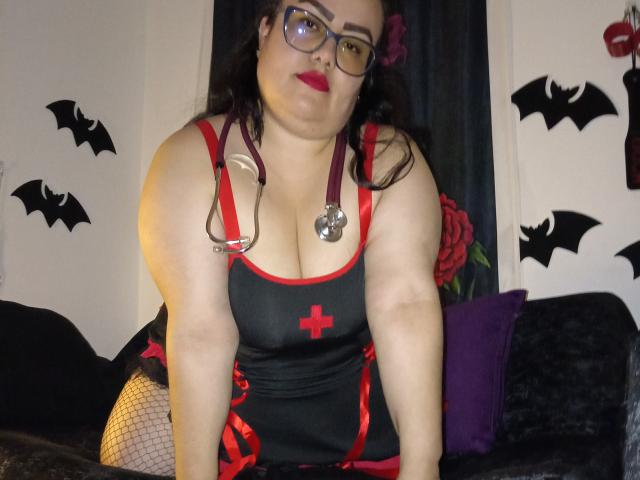 FoxyBell a de grandes seins, elle porte une robe d'infirmière avec une croix rouge, des bretelles rouges, des bas de pêche noirs et des lunettes, avec un stéthoscope, du rouge à lèvres et un corps voluptueux et de grande taille..
