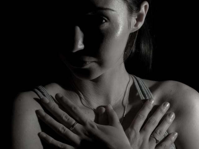 ChloeSensual's face is partially shadowed, with her hands covering her chest, showing her shiny, sweaty skin and a necklace. Her tits are slightly visible under her tank top.